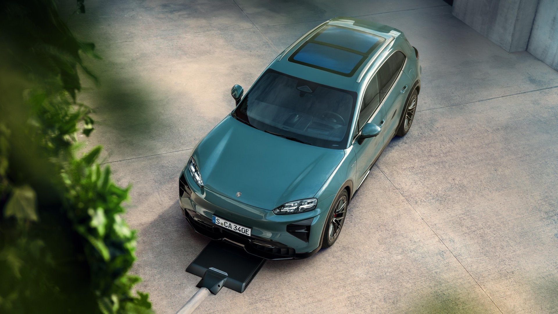 Top-down view of the 2026 Porsche Cayenne Turbo Electric using a wireless charging pad, showcasing its panoramic roof and aerodynamic shape.