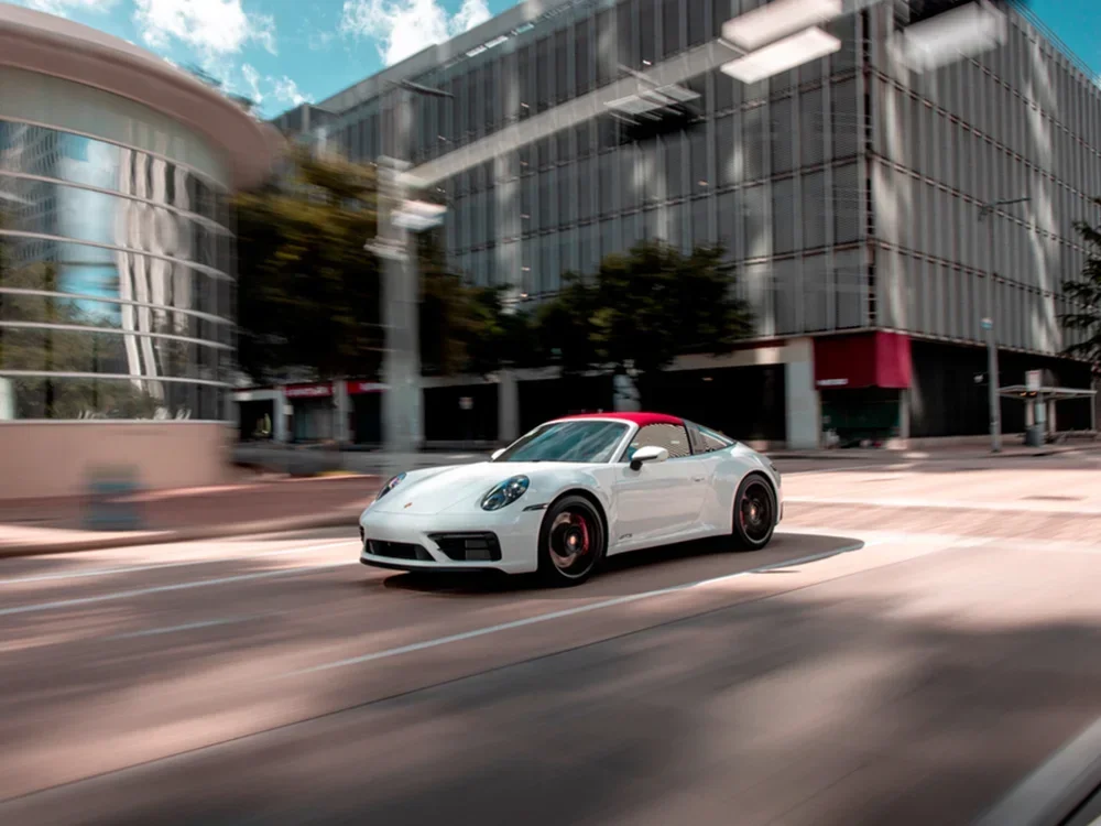 White Porsche 911 with black wheels and red calipers driving through the streets of downtown Denver